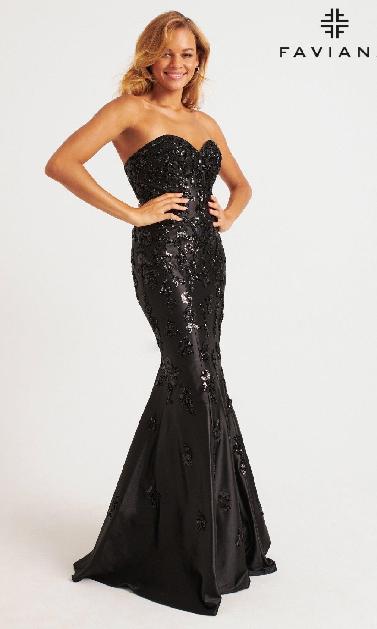 A woman stands smiling in the Long Prom Dress: Faviana 11271—strapless, black, mermaid style with sequin and floral details.